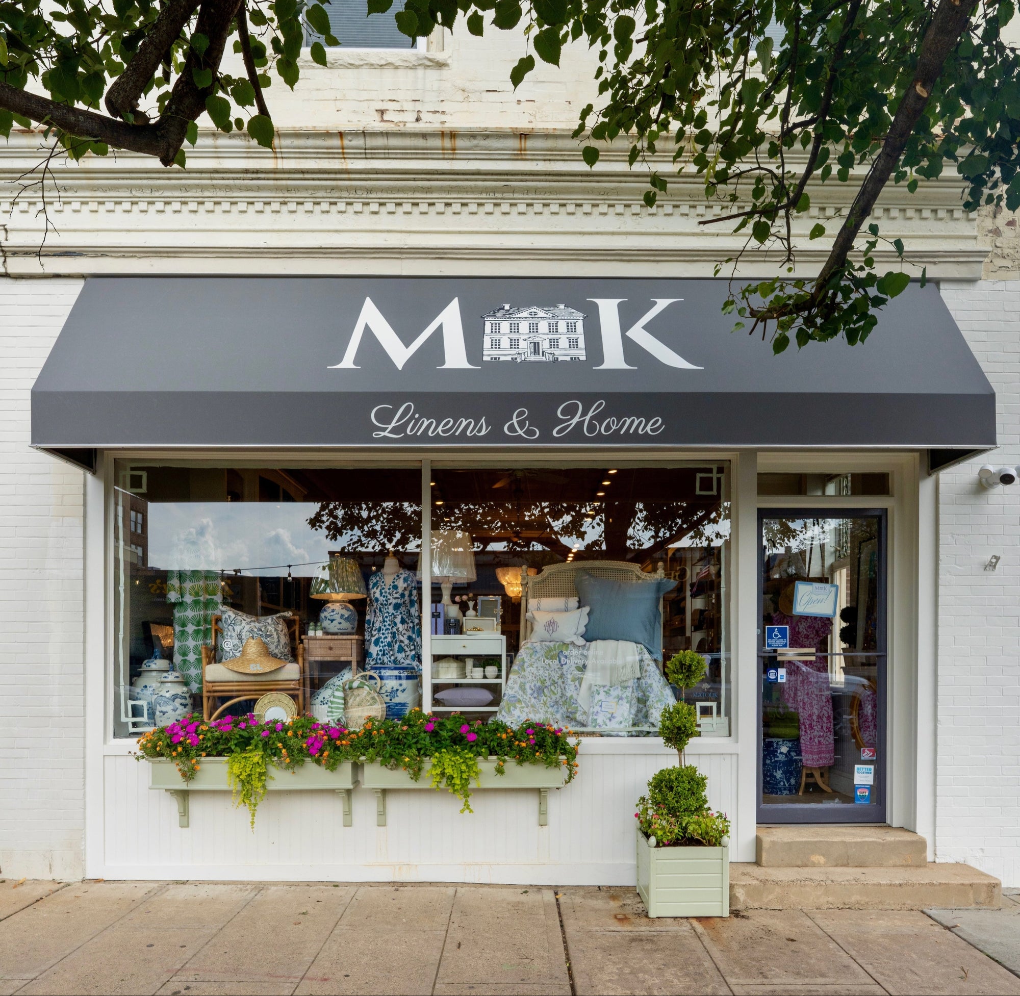 Storefront with 'MK Linens & Home' sign under a tree